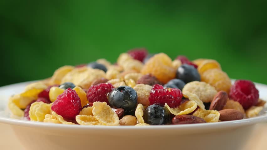 Pour milk on crunchy granola cereals. Morning eating with flakes, raspberries, blueberries, nuts, oatmeal. Healthy breakfast concept, Healthy food, clean eating, closeup, rotation background | Shutterstock HD Video #1108784217