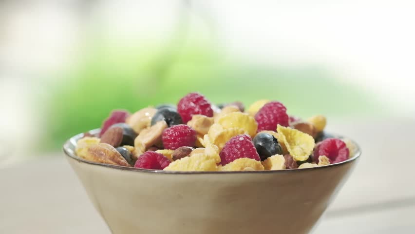 Pour milk on crunchy granola cereals. Morning eating with flakes, raspberries, blueberries, nuts, oatmeal. Healthy breakfast concept, Healthy food, clean eating, closeup, rotation background | Shutterstock HD Video #1108784219