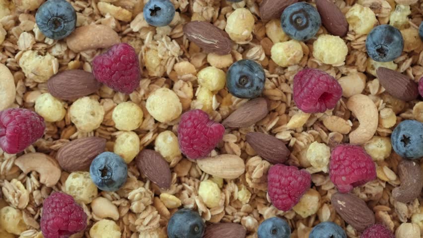 Pour milk into the bowl full of crunchy granola cereals. Morning eating with healthy flakes with raspberries, blueberries, nuts, oatmeal. Healthy breakfast concept, Healthy food, clean eating, closeup | Shutterstock HD Video #1108784223