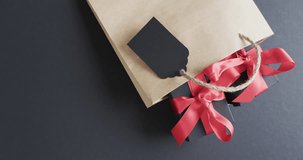Video of gift bag, gift tag and gift boxes with red ribbon and copy space on black background. Cyber monday, black friday, online shopping, shipping and global connections concept.