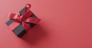 Video of gift box with red ribbon and copy space over red background. Cyber monday, black friday, online shopping, shipping and global connections concept.