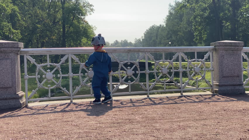 toddler child little boy on white bridge in the park looks at wild ducks. Aleksandrovsky Park, Pushkin, St. Petersburg, Russia.