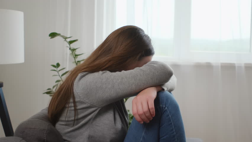 Upset young caucasian woman frustrated by problem with relationships, sitting on sofa, embracing knees, covered face in hand, feeling despair and anxiety, loneliness, having psychological trouble Royalty-Free Stock Footage #1108797689