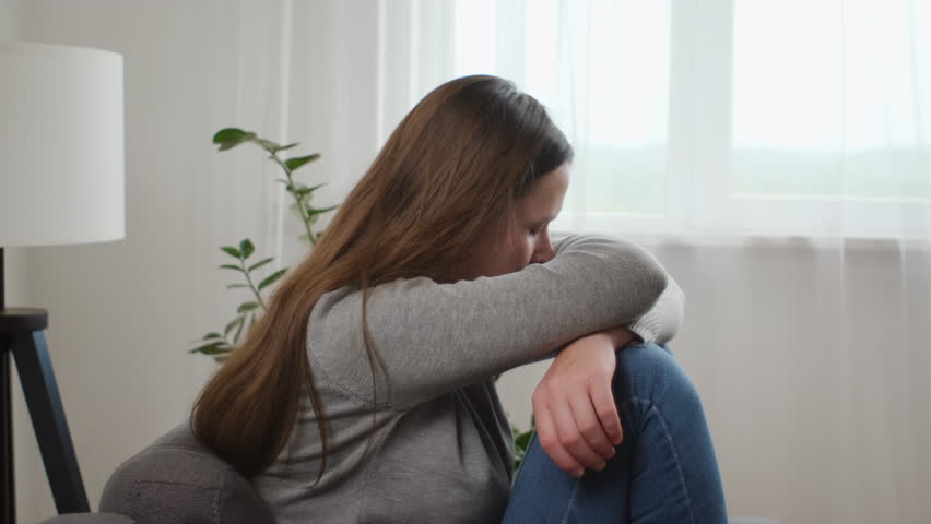 Upset young caucasian woman frustrated by problem with relationships, sitting on sofa, embracing knees, covered face in hand, feeling despair and anxiety, loneliness, having psychological trouble | Shutterstock HD Video #1108797689