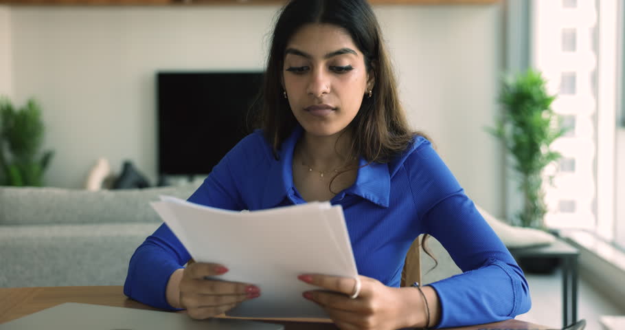 Serious Indian woman sit at desk hold documents read bad news, eviction notification, feels desperate about financial problems. Young female student worried college expulsion, failed exam test results Royalty-Free Stock Footage #1108798145