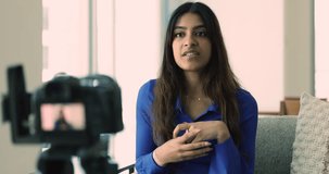 Young Indian woman sit on sofa make speech, talking, records new videoblog, video for channel for social media blog, express thoughts, share experience with subscribers use professional digital camera