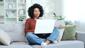 Young african american woman freelancer talking on a video call using a laptop sitting on couch in home office. Black woman student communicates at an online meeting, has a consultation with a tutor