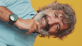 Vertical video, Close-up of an elderly gray-haired bearded man wearing a blue shirt, looking camera, thinking pleasant, smiling, isolated on an orange background in the studio - Powered by Shutterstock - Get 15% off with code: PIKWIZARD15