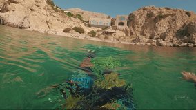 POV shot, man paddling with his fins underwater sailing away from beautiful rocky shore. First person video, guy swims on surface in water of Mediterranean sea