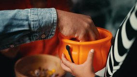 Mom and dad put candy into little son's trick or treat basket, Halloween customs. African American family dressed in costumes spend time together at home and celebrate Halloween holiday - Powered by Shutterstock - Get 15% off with code: PIKWIZARD15