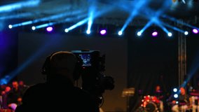 At an outdoor concert, cameras are recording. We see the movement of the camera from the cameraman's perspective.