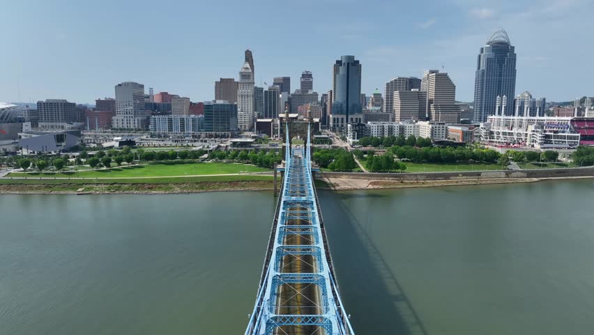 John A. Roebling Suspension Bridge in downtown Cincinnati, Ohio over the Ohio River. Aerial establishing shot on beautiful summer day with city skyline in the distance.
