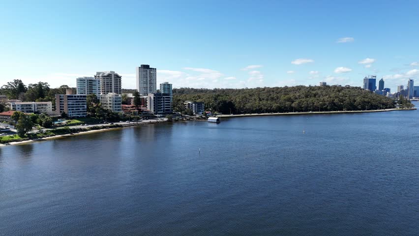 Blue boat house in Perth, Western Australia with traffic driving past in the back ground along the Swan River.