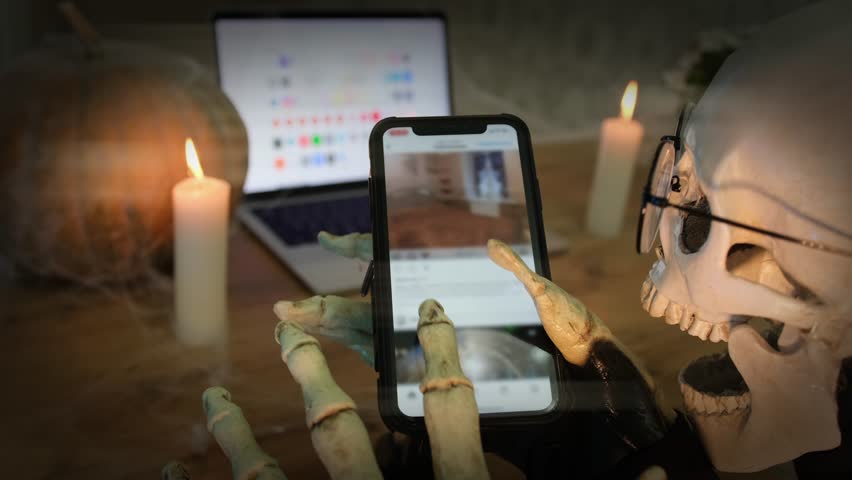 Festive background to Happy Halloween, spooky holiday atmosphere. Close up, hands in skeleton costume holding for smartphone scrolls social networks. Halloween party, social media. | Shutterstock HD Video #1108822843