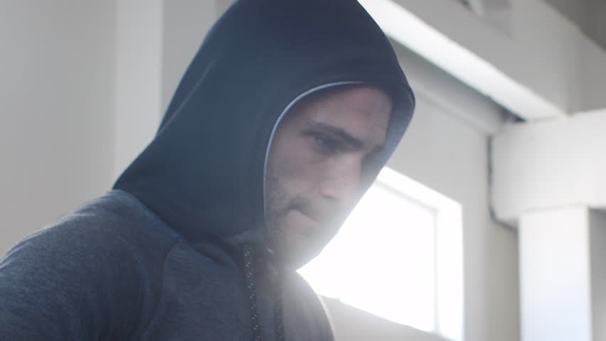 Closeup of thoughtful athlete looking down while walking in gym. Young male is wearing hooded shirt. He is serious while working out in healthcare centre.