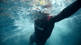 Underwater view of professional swimmer training in swimming pool, 4k 120 fps super slow motion raw video. Triathlete swim in black wetsuit 