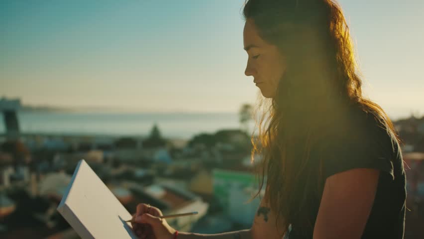 Woman Artist by City River in Gold Sunlight Drawing Pencil Art on Canvas. Alone Europe Designer Painting at Pretty Terrace Using Calm Emotions of Shine Sky Set. Person with Long Hair in Casual Clothes Royalty-Free Stock Footage #1108827677