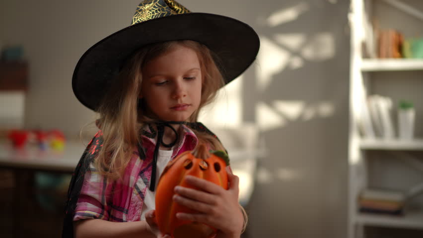 Portrait of cute Caucasian charming girl in Halloween costume with Jack O lantern indoors. Confident pretty child getting ready for holiday celebration on October 31 Royalty-Free Stock Footage #1108828817