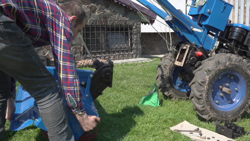 installation of the cultivator to the tractor,an older man and his son are installing a milling cutter to a walk-behind tractor