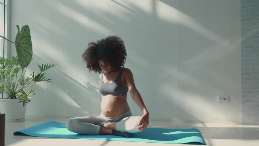 African young adult pregnant woman in workout clothes exercising, yoga and Practice meditation by window and basking in the warm morning sunlight to maintain health and well-being during pregnancy Royalty-Free Stock Footage #1108829885