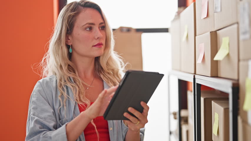 Young blonde woman ecommerce business worker using touchpad checking packages at office