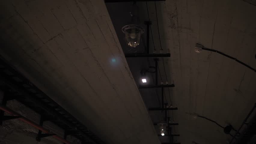 A long winding tunnel with old lamps and wires. A dark corridor with flashing and broken lamps on the ceiling, a creepy place underground, catacombs. Nuclear war, bomb shelters, underground tunnel.