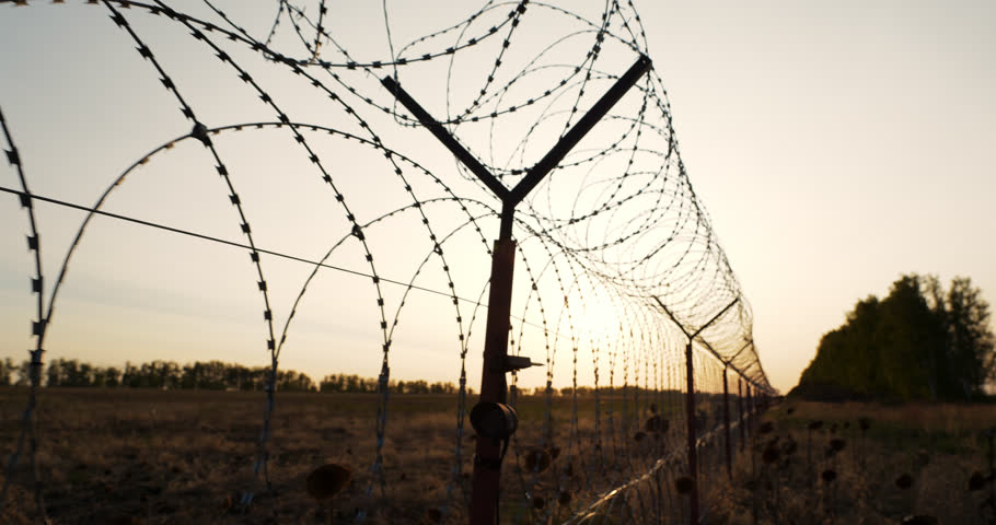 High barbed wire fence protect private country facility or military zone, boundary barrier restrict prison isolated base at sunset close up. Border line control and closed perimeter for secure Royalty-Free Stock Footage #1108834547