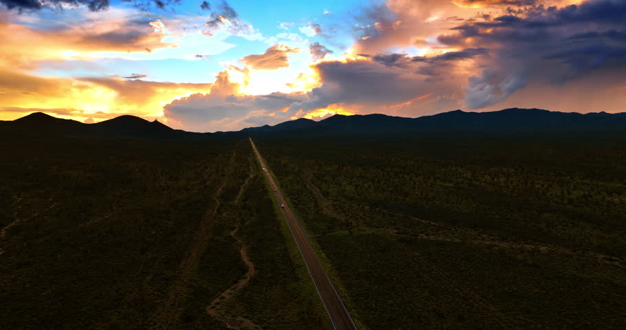 Straight highway passing the Death Valley after sunset. Cars with headlights on run by the roads. Beautiful colorful sky at backdrop.