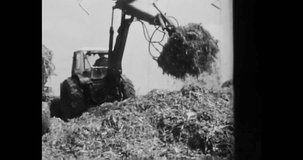 Tractor working on collective farm. Tractor carrying, shoveling, loading hay corn. 1970 USSR Ukraine. Farmer machine in rural scene. farmland combine. Vintage black white archival film. Retro archive