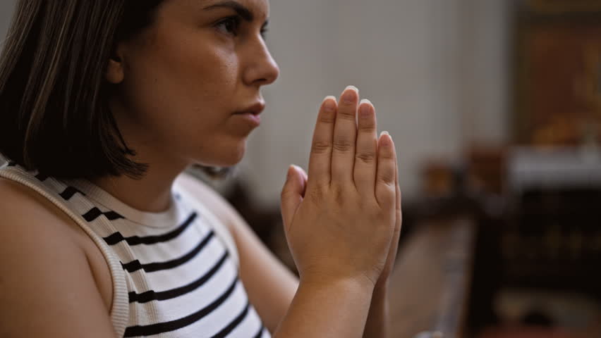 Young beautiful hispanic woman praying on a church bench at Augustinian Church in Vienna