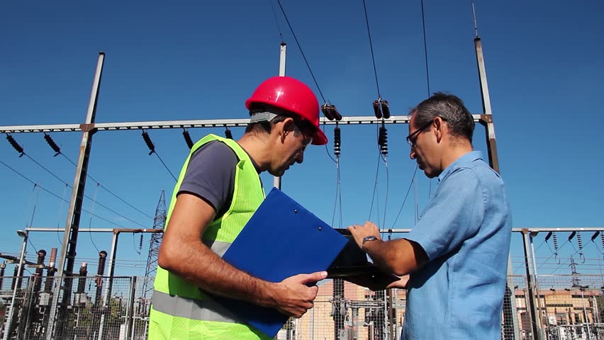 Power Distribution Supervisor and Electricity Distribution Worker at Electrical Substation. Electrical Engineer and Power Line Worker Discussing Plan of Work Next to High Voltage Substation. Royalty-Free Stock Footage #1108838483