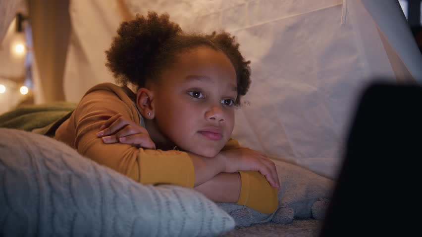 Girl at home lying inside indoor tent or camp watching or streaming to digital tablet - shot in slow motion