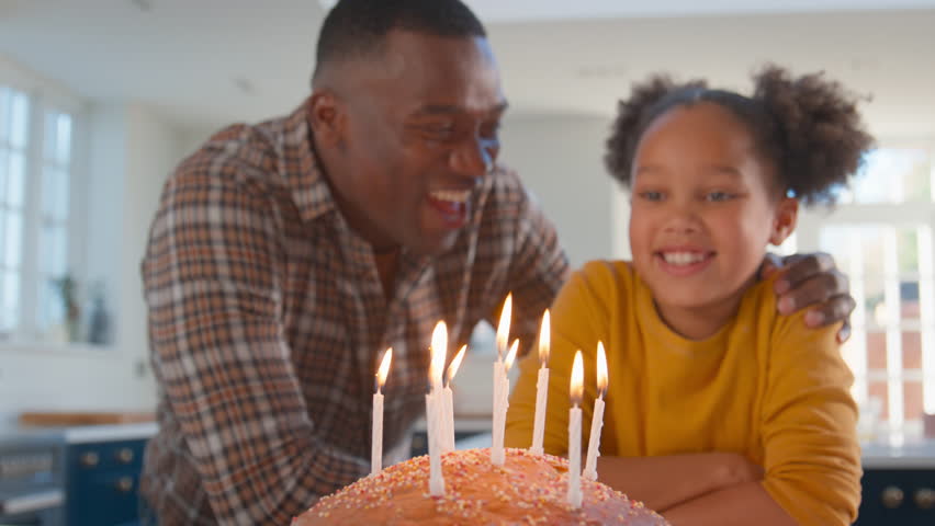 Father and daughter at home in kitchen celebrating blowing out candles on homemade birthday cake - shot in slow motion