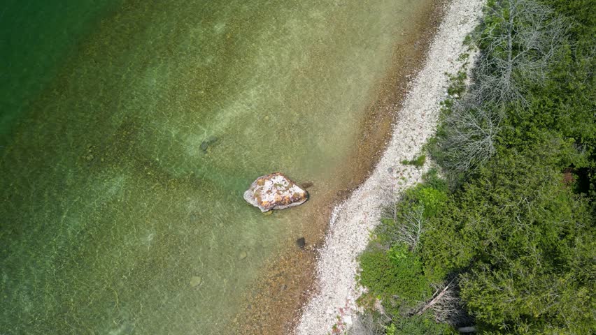 Aerial down view of large rock along forested coastline, Michigan, Lake Huron