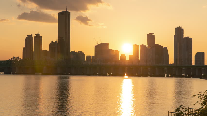 Seoul City Sunset With Sun Hiding Behind Yeouido Island Buildings During Golden Hour Time. Hangang Waterfront Landscape Timelapse, Train Moving on Railway Bridge Over Han River