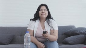 Asian fat woman Drink water while watching TV on the sofa at home.