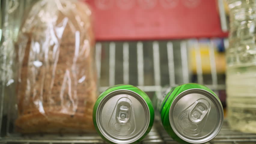 Close-up of male hand putting golden cans of beer into a shopping cart on a store