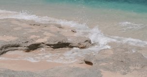 Meditation video and travel background. An ocean wave rolls onto the stones that lie on the shore and splashes in different directions. Wave splash and foam from the ocean. Blue ocean water, beach.