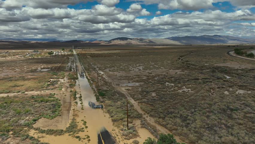 Flooded Mojave Desert road after unseasonal torrential rains leaves a vehicle stranded - aerial parallax