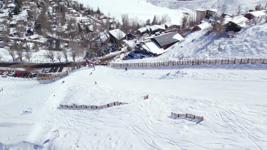 Aerial orbit of a person ascending the Farellones ski slope through the t-shaped drag lift, parallax effect of the snowy village of Farellones. Royalty-Free Stock Footage #1108853313
