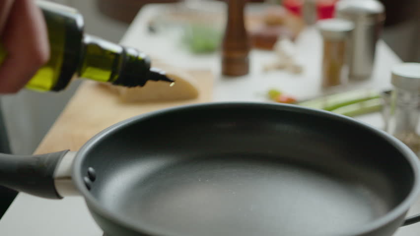 Close-up view of hand of chef pouring olive oil on frying pan before cooking food in the kitchen