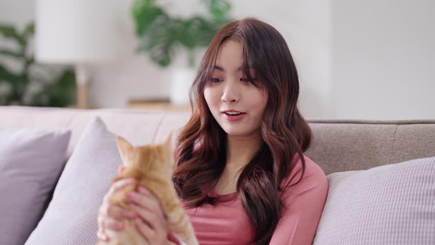 happy asian woman with lovely pet kitten ginger cat at home
