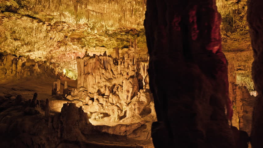 Underground cave with distinct rocky formations of stalactites and stalagmites. A colourful natural scenery in a cave with ancient cavities formed of carbonate limestone rocks in Mallorca, Spain. Royalty-Free Stock Footage #1108858977
