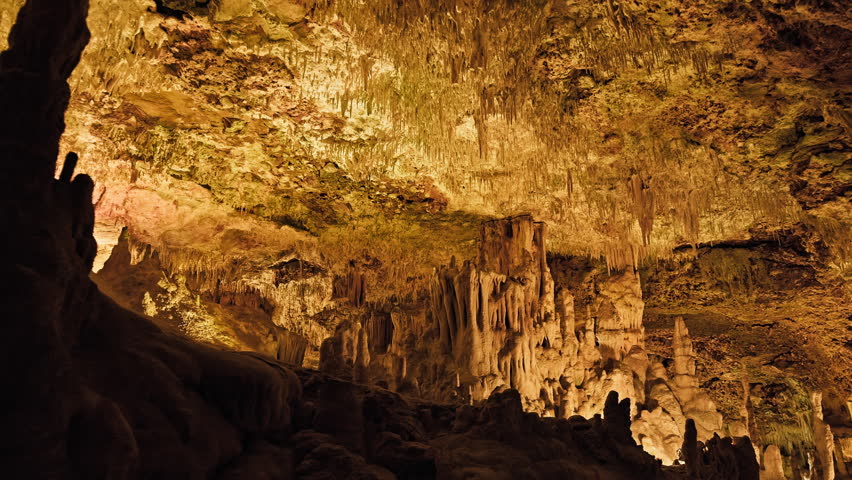 Underground cave with distinct rocky formations of stalactites and stalagmites. A colourful natural scenery in a cave with ancient cavities formed of carbonate limestone rocks in Mallorca, Spain. Royalty-Free Stock Footage #1108858979