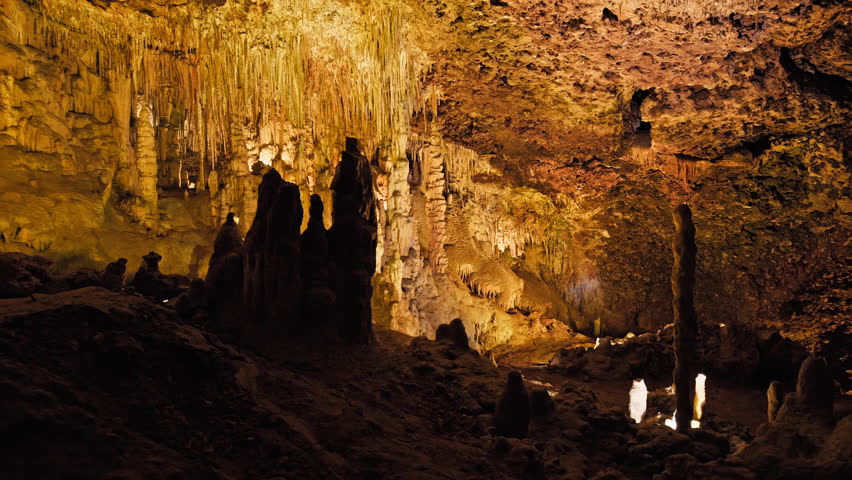 Underground cave with distinct rocky formations of stalactites and stalagmites. A colourful natural scenery in a cave with ancient cavities formed of carbonate limestone rocks in Mallorca, Spain. Royalty-Free Stock Footage #1108858981