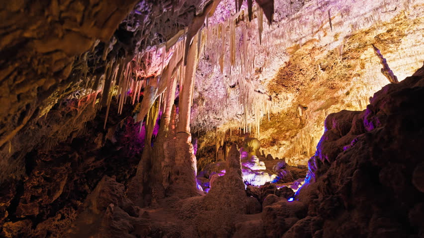Underground cave with distinct rocky formations of stalactites and stalagmites. A colourful natural scenery in a cave with ancient cavities formed of carbonate limestone rocks in Mallorca, Spain. Royalty-Free Stock Footage #1108859005