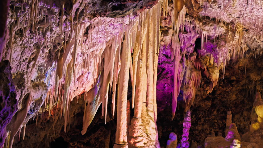 Underground cave with distinct rocky formations of stalactites and stalagmites. A colourful natural scenery in a cave with ancient cavities formed of carbonate limestone rocks in Mallorca, Spain. Royalty-Free Stock Footage #1108859007