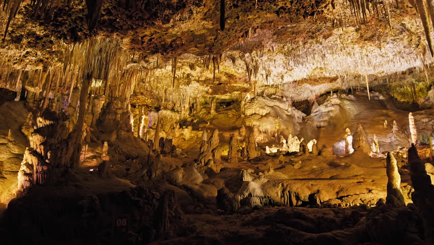 Underground cave with distinct rocky formations of stalactites and stalagmites. A colourful natural scenery in a cave with ancient cavities formed of carbonate limestone rocks in Mallorca, Spain. Royalty-Free Stock Footage #1108859013