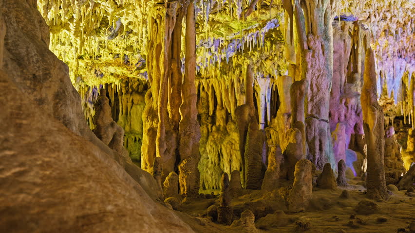 Underground cave with distinct rocky formations of stalactites and stalagmites. A colourful natural scenery in a cave with ancient cavities formed of carbonate limestone rocks in Mallorca, Spain. Royalty-Free Stock Footage #1108859015
