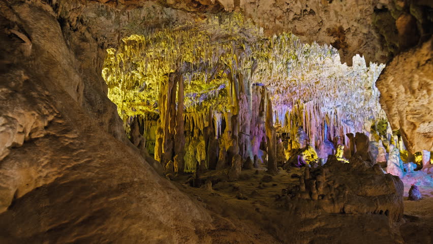 Underground cave with distinct rocky formations of stalactites and stalagmites. A colourful natural scenery in a cave with ancient cavities formed of carbonate limestone rocks in Mallorca, Spain. Royalty-Free Stock Footage #1108859023